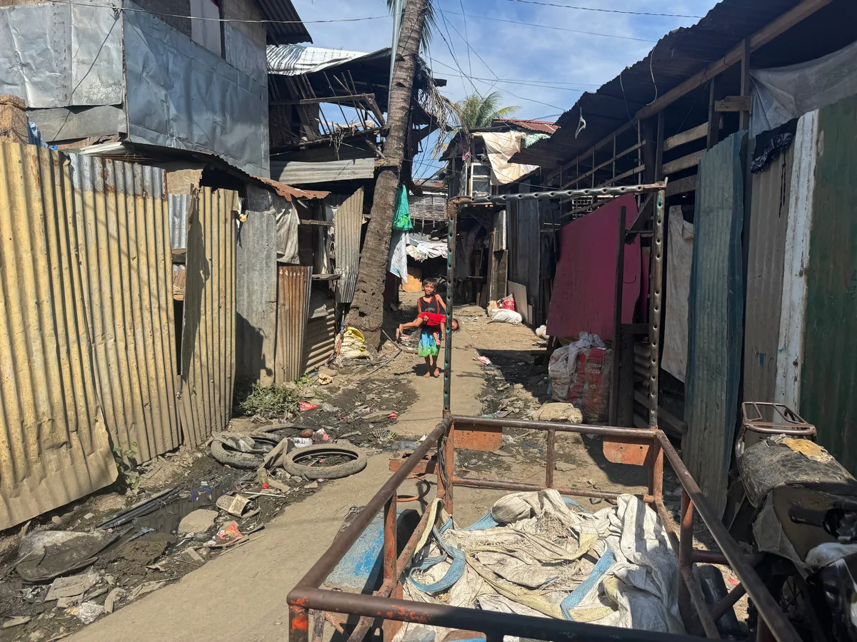 Zwischen Müllbergen reihen sich Wellblechhütten aneinander. Ein Kind trägt sein Geschwister durch die Gassen der Mülldeponie.